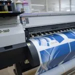 a large format printing machine with a printed sheet of white vinyl printed with blue graphics